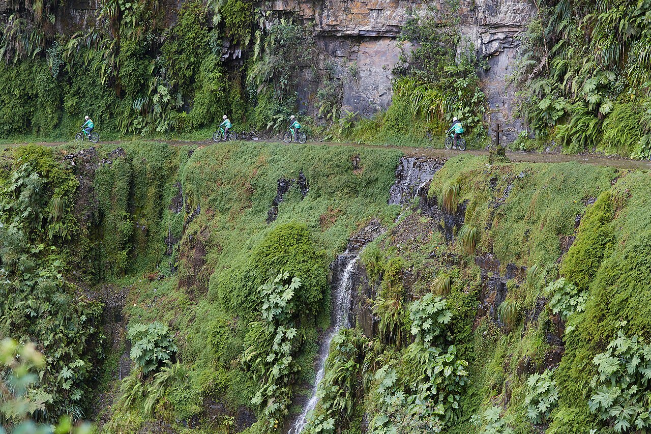 Mountainbikers op de smalle Yungas Road langs een groene rotswand en waterval